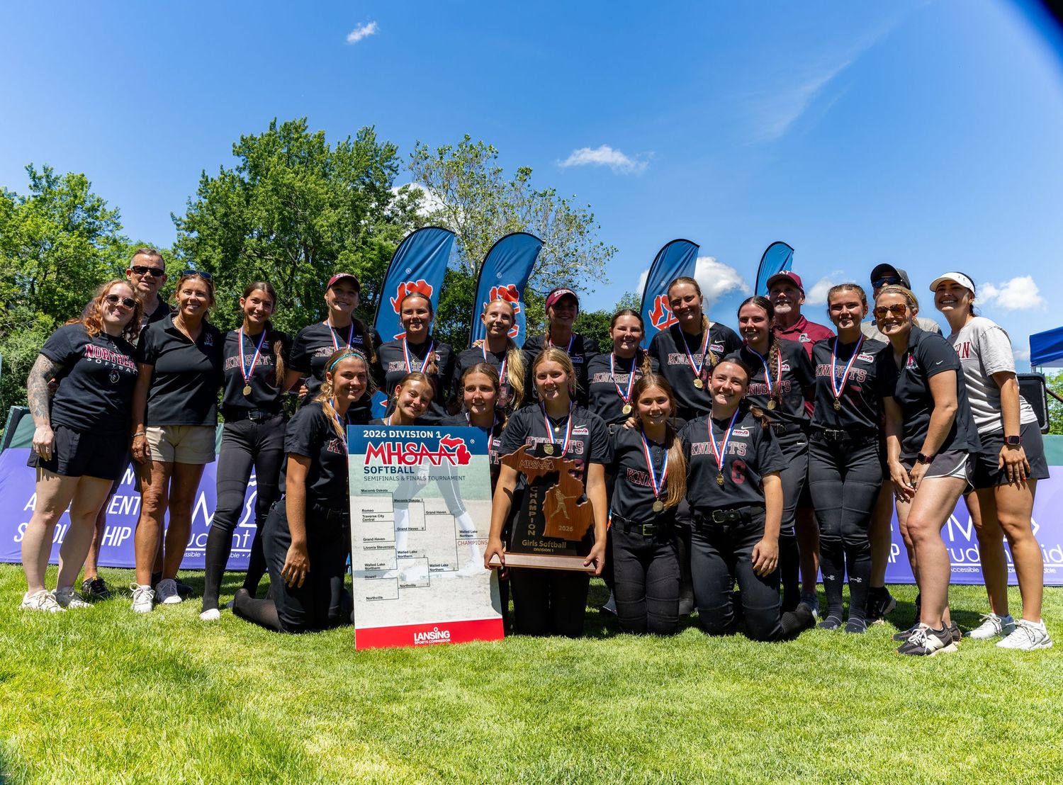 Youth baseball team celebrates with championship banner on baseball field.