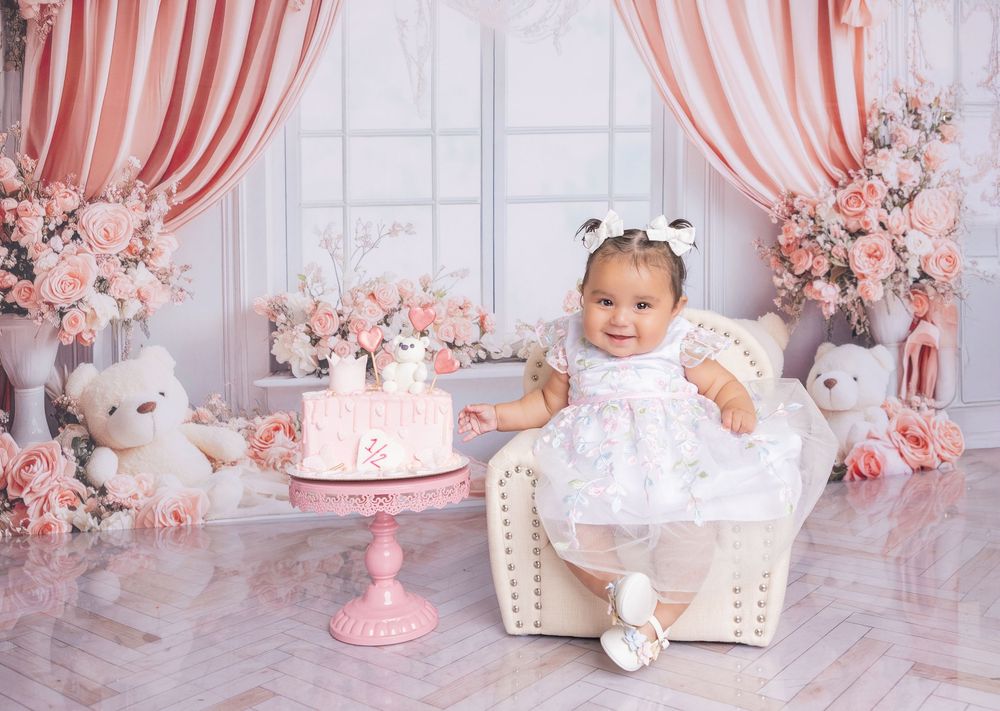Pink and white first birthday cake smash photo session with floral decorations and white wicker chair.