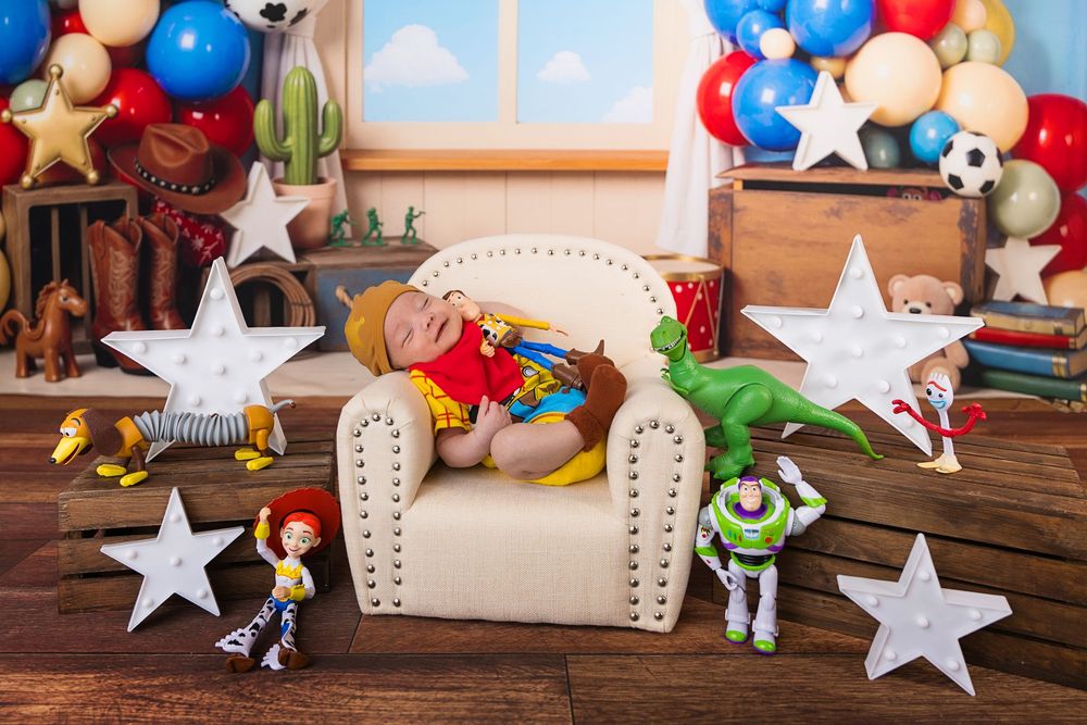 Newborn baby sleeping on mini sofa surrounded by Toy Story characters Woody Jessie Buzz Rex with star props and balloons.