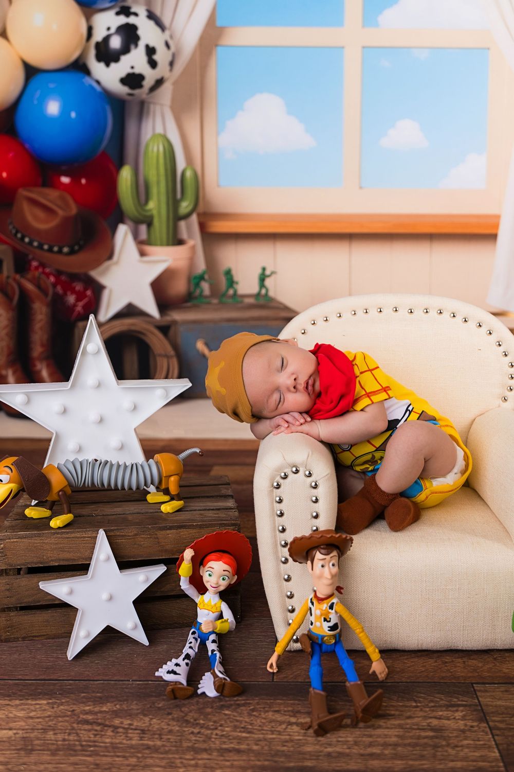 Sleeping newborn dressed as Woody from Toy Story on mini armchair with Jessie and Woody dolls and western-themed decorations.