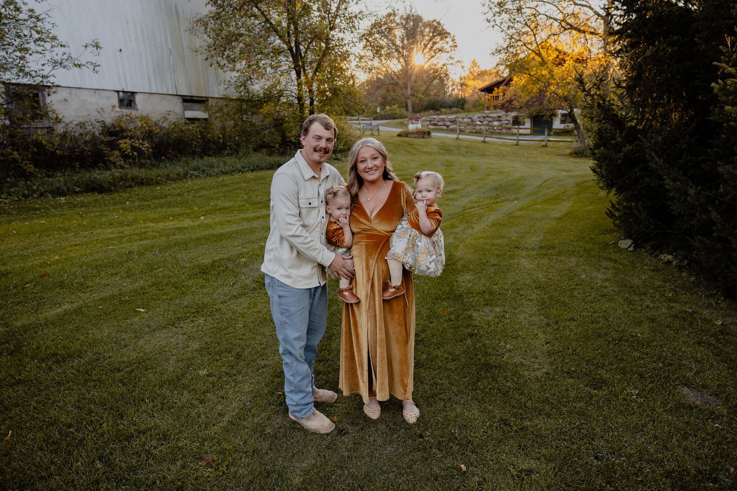 A family with young twins pose together in a grassy field during golden hour with autumn trees in the background in Saukville, WI with ERP!