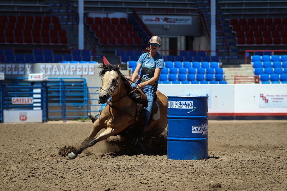 Horse and rider racing around blue barrel during rodeo competition in stadium arena.