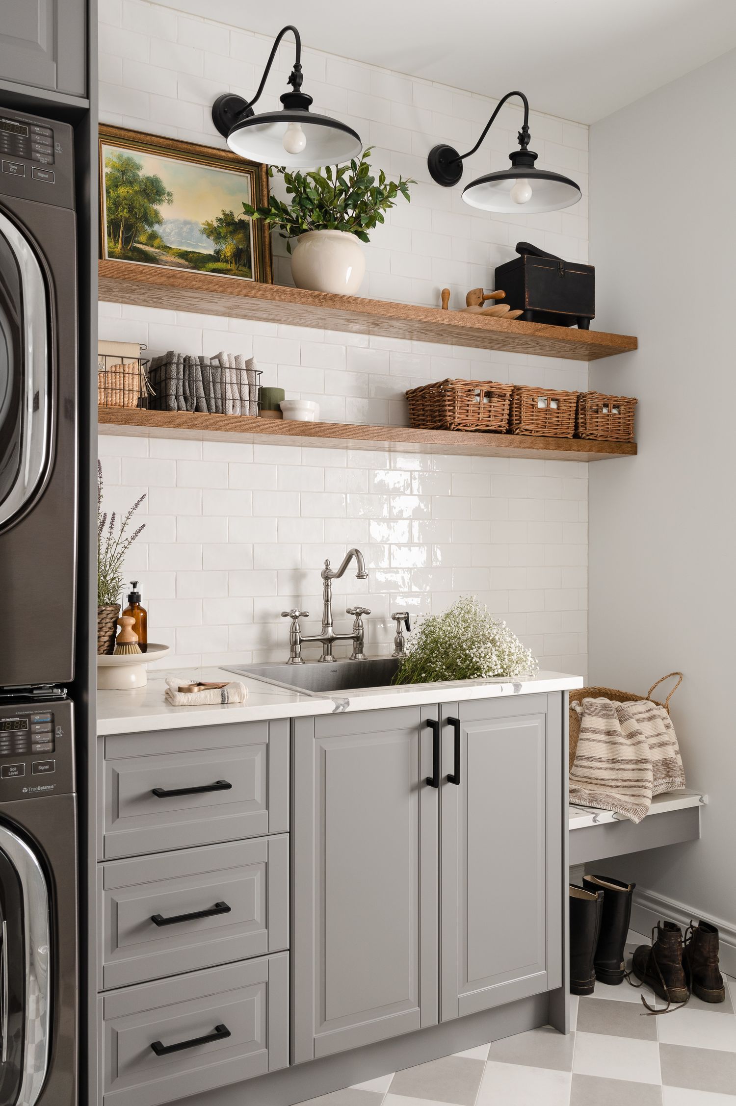 Gray laundry room with subway tile backsplash, floating wooden shelves, and black sconce lighting.