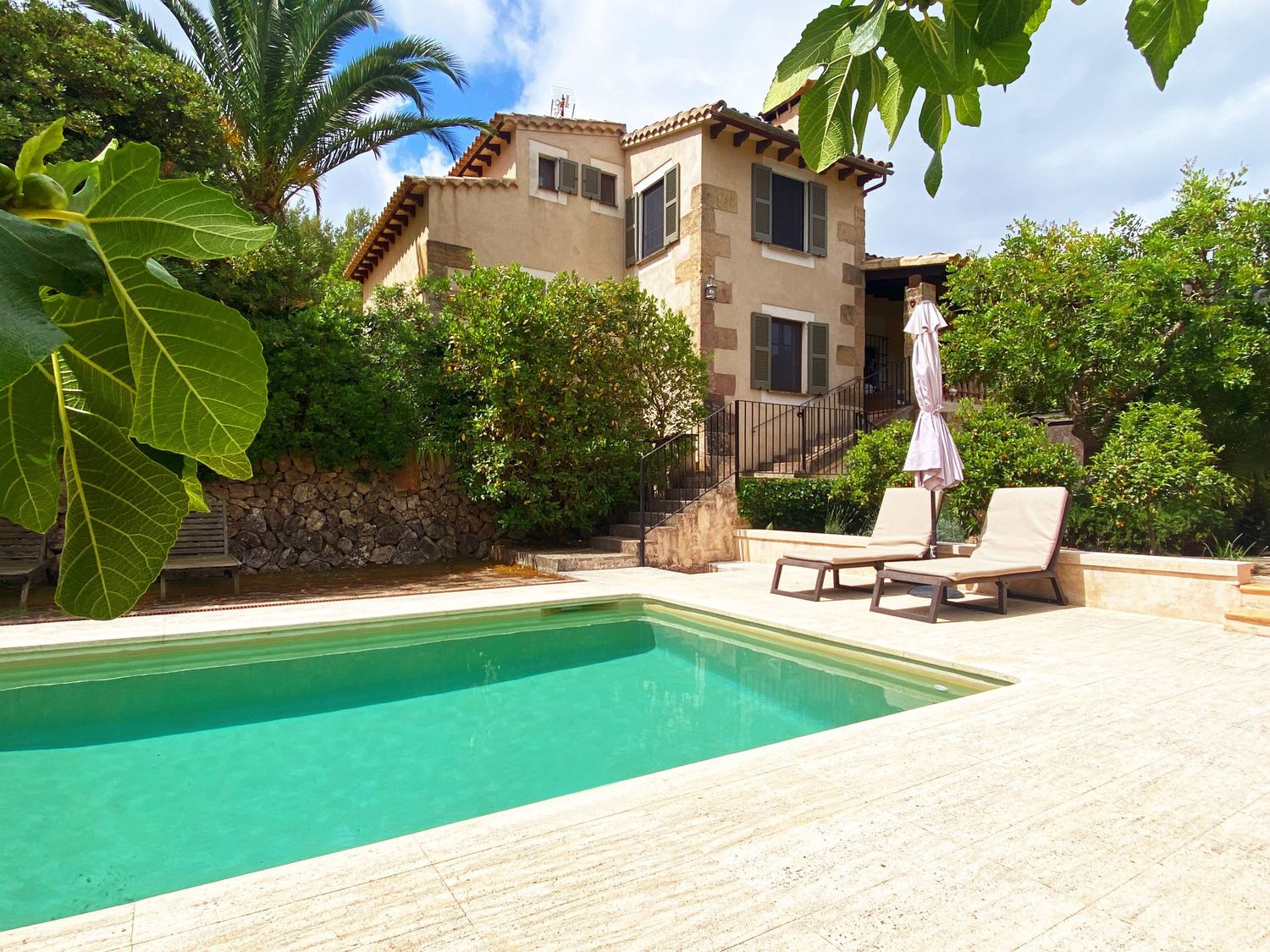 Mediterranean villa with turquoise swimming pool surrounded by lush gardens and palm trees.