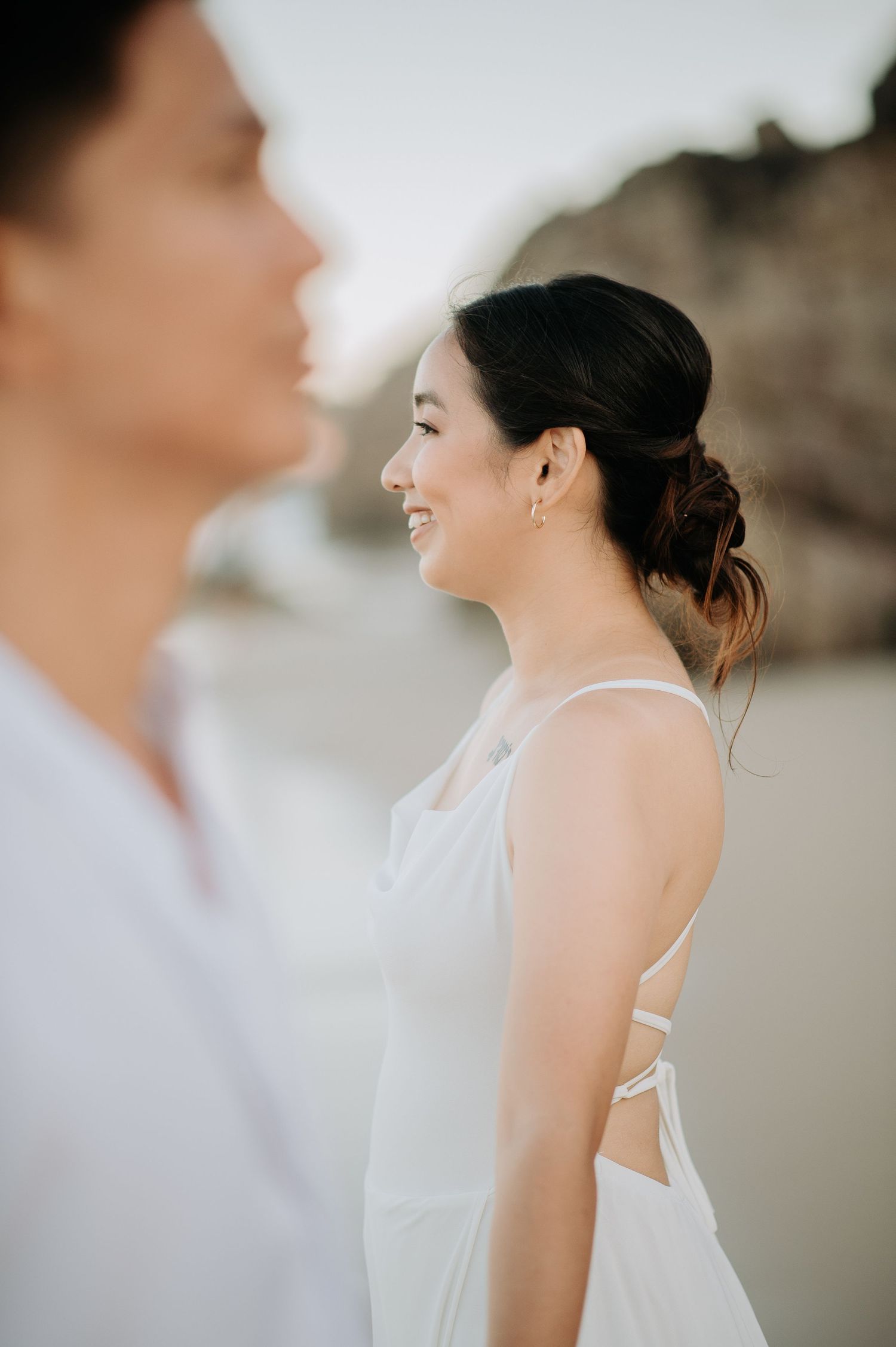 Side profile portrait of a couple in wedding attire against a blurred beach background.