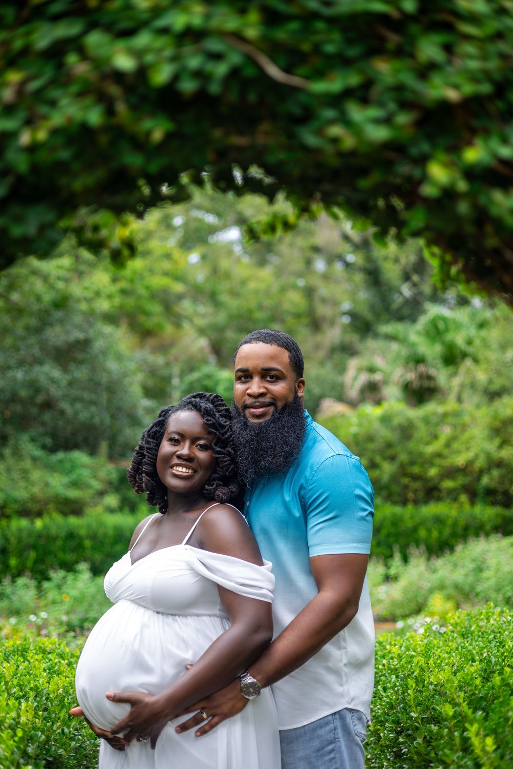 Maternity photo of couple embracing in lush garden setting.