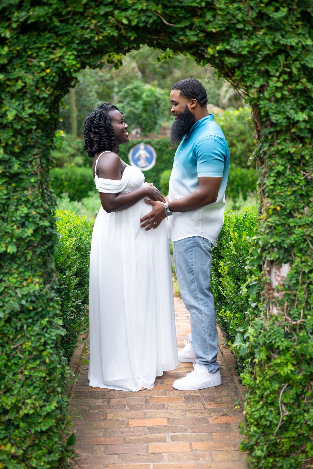 Expecting couple shares intimate moment under garden archway framed by greenery.