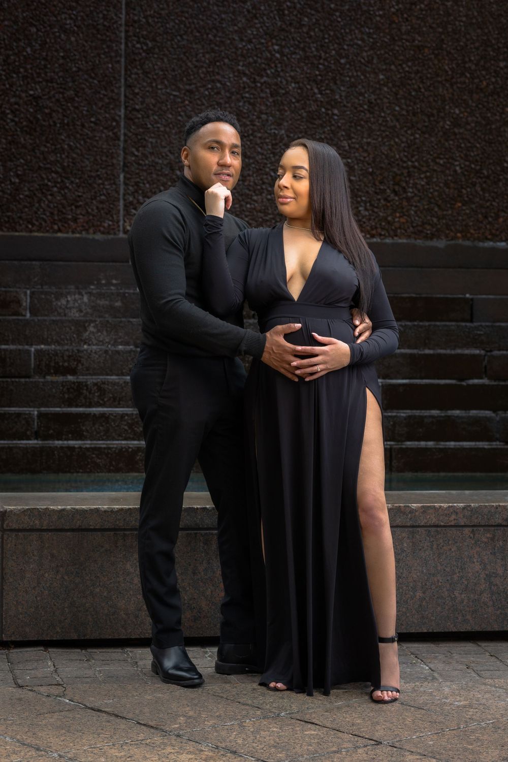 A couple poses on stone steps wearing coordinated black formal wear.