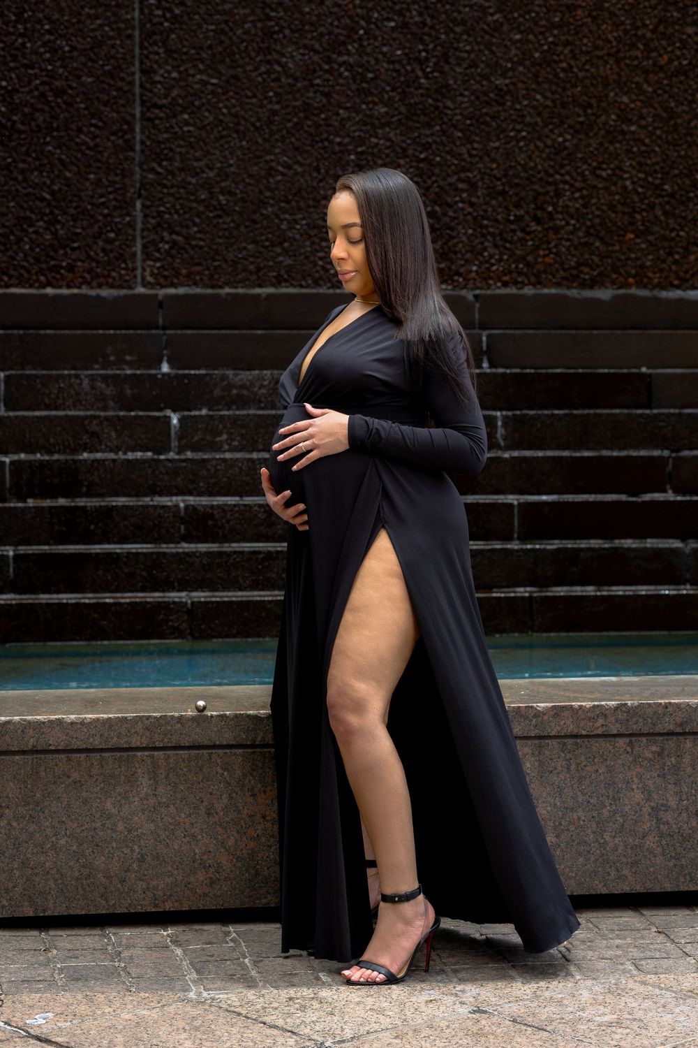 Stylish maternity portrait showcasing black maxi dress with slit against dark background.