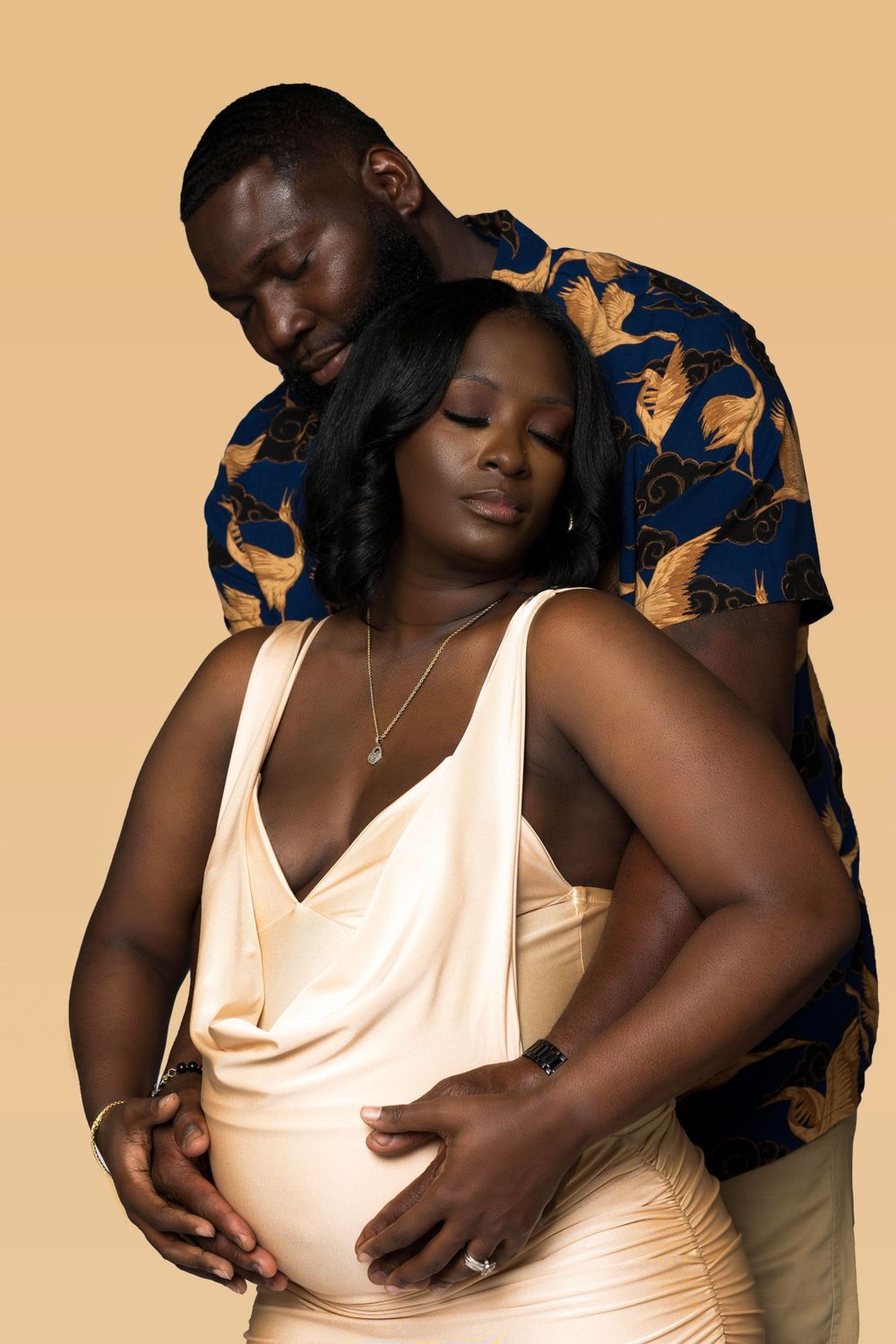 Intimate maternity photo of couple embracing in cream and navy against beige background.