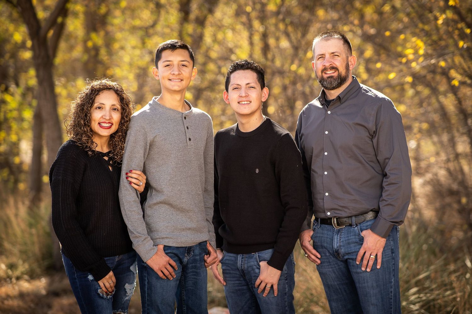 Family of four poses together outdoors during autumn with fall foliage in background.