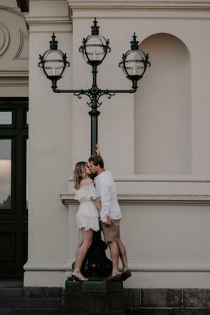 A couple kissing while holding onto a lamp pole.