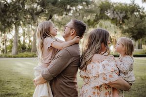 Family shares tender moments together in a sunlit outdoor setting wearing coordinated neutral and floral outfits.