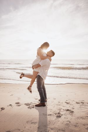 Romantic couple embracing on a misty beach at sunset with waves crashing in the background after their breathtaking engagement session.
