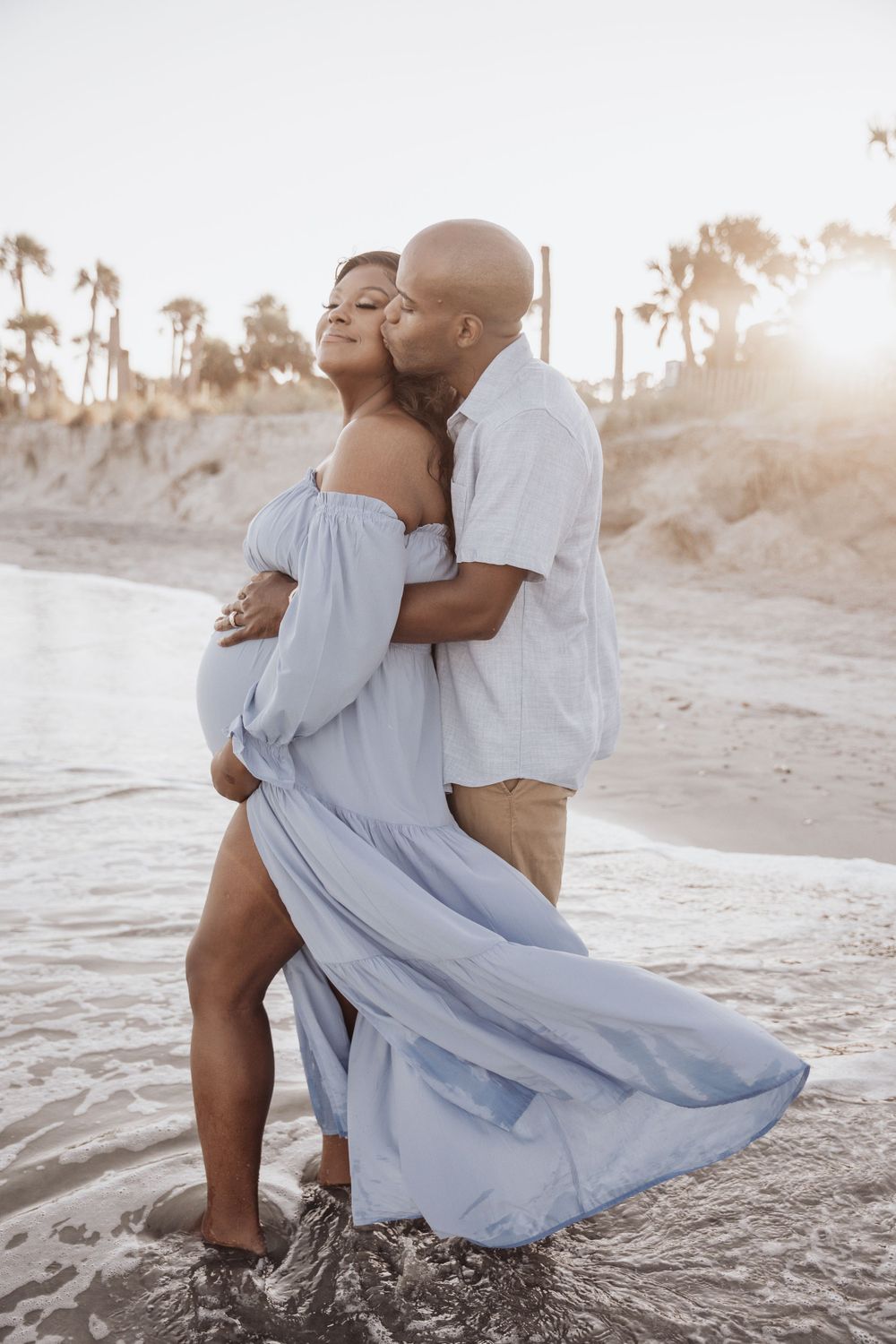 A romantic couple embraces on a sun-drenched beach with palm trees silhouetted in the golden hour light.