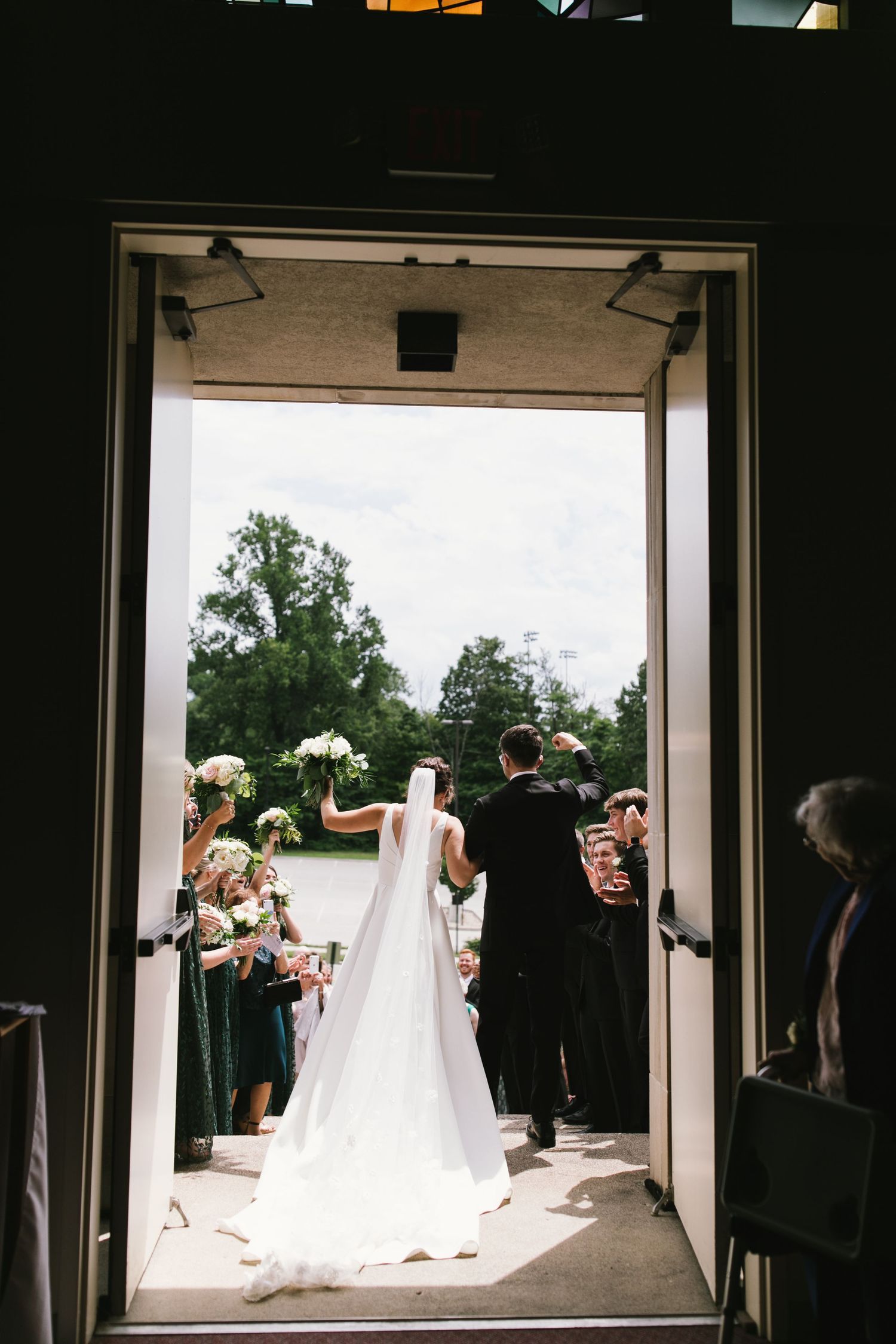 Wedding ceremony exit captured through doorway showing trailing white bridal veil.