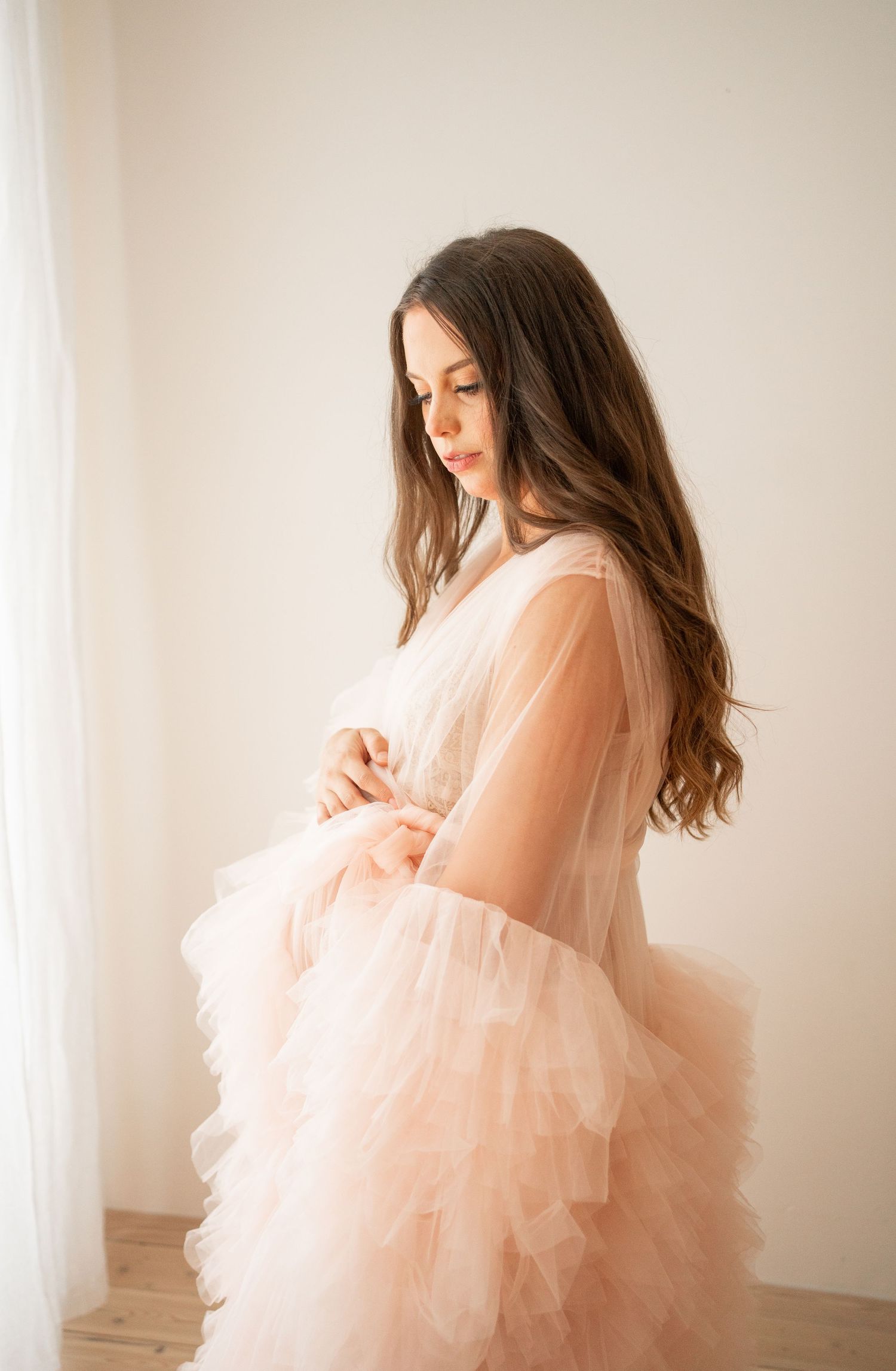 Dreamy maternity portrait in peach tulle dress by window light.