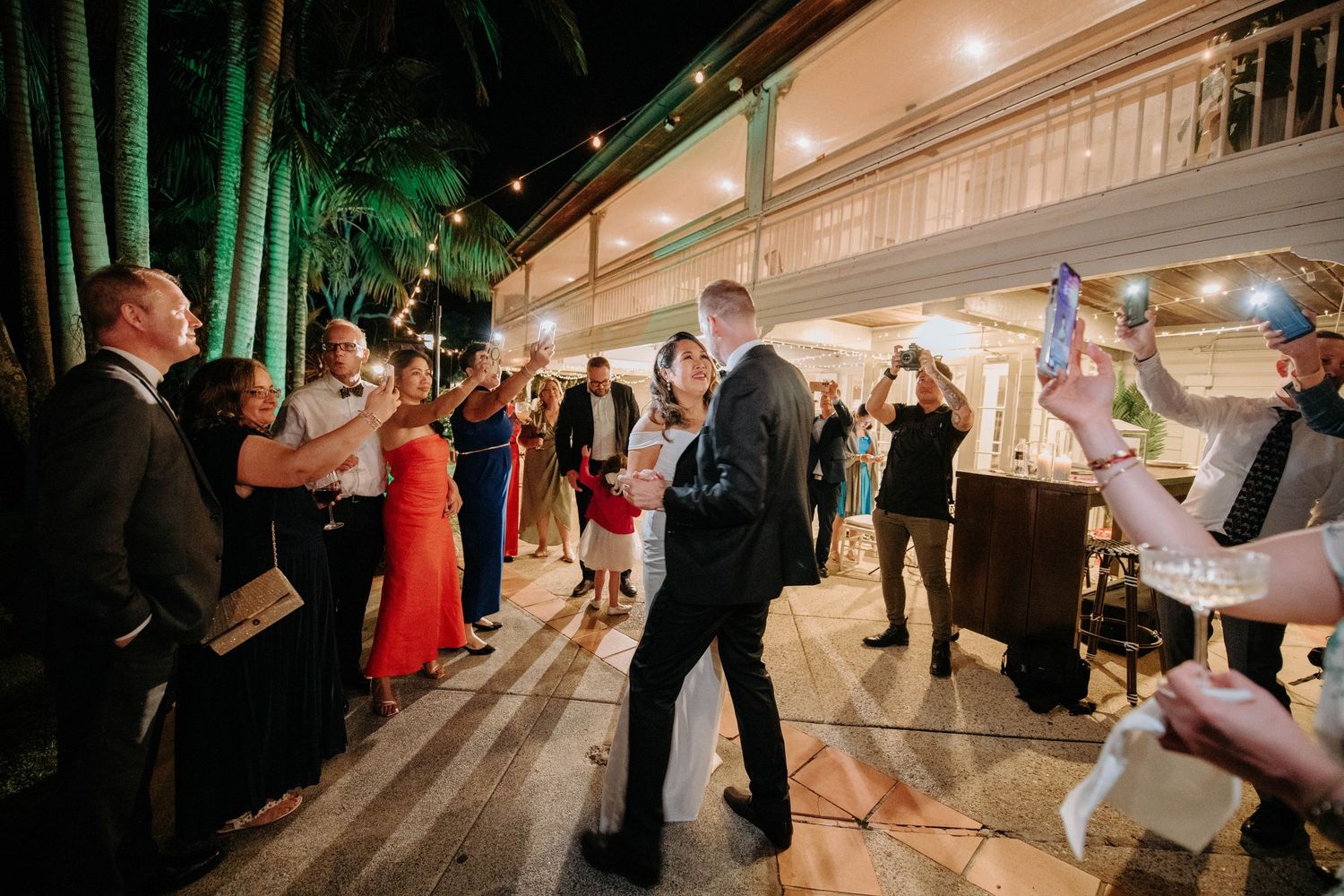 Wedding reception guests dancing and celebrating on an outdoor patio with string lights.
