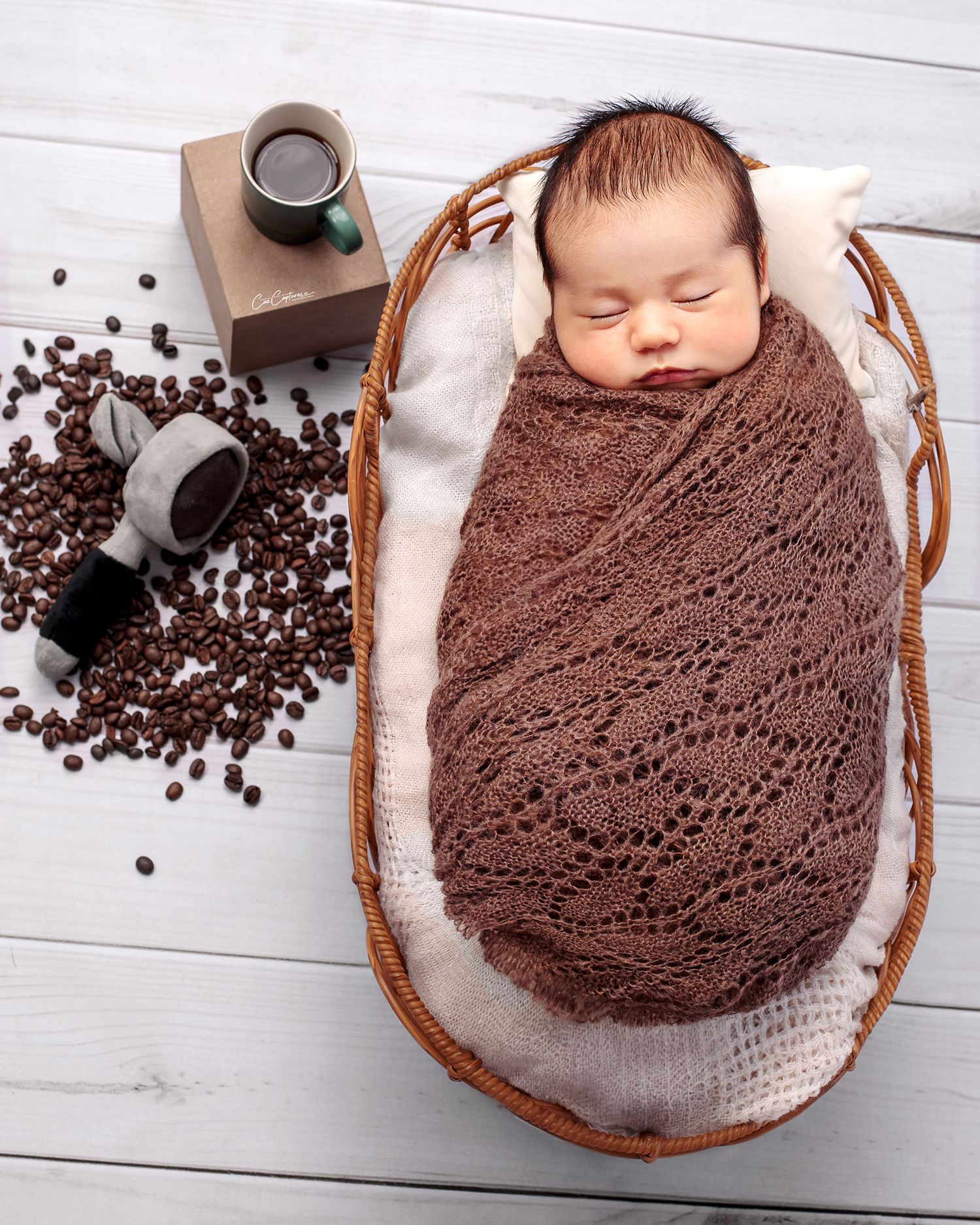Coffee themed Newborn portrait of baby boy wrapped in brown blanket on basket next to him a espresso coffee and coffee beans.