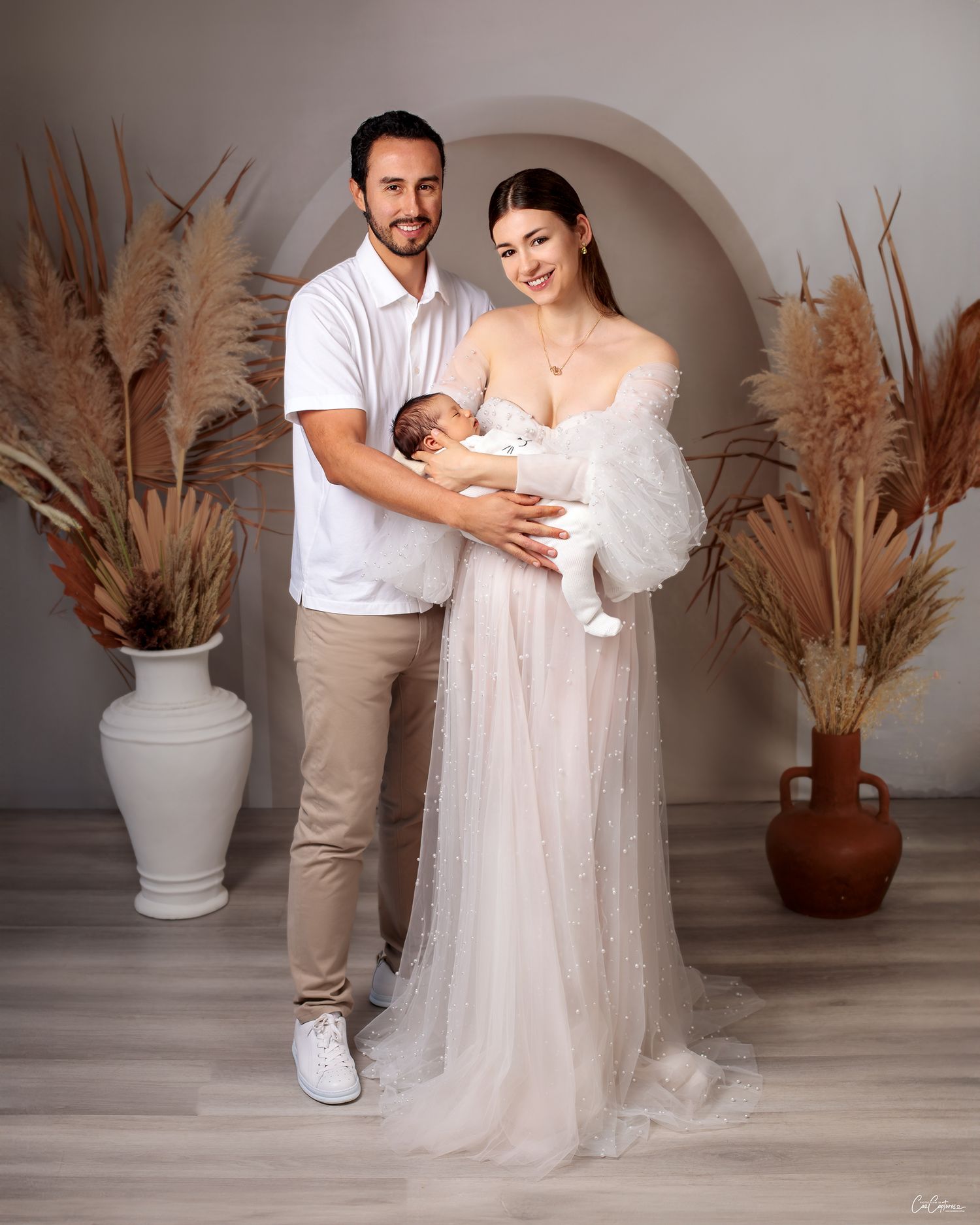 mum and dad standing together smiling holding their newborn baby boy, mother in couture pearl gown by Caz Captures Sydney Photographer
