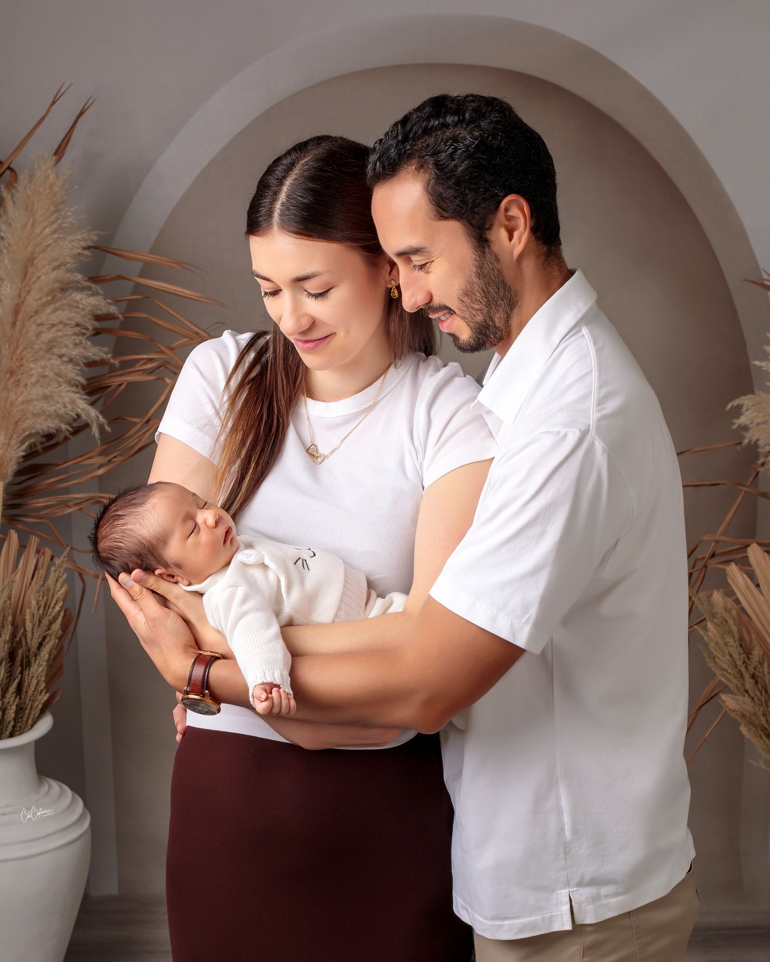 Close up of a mum and dad huddled together smiling holding their newborn baby boy by Caz Captures Sydney Photographer