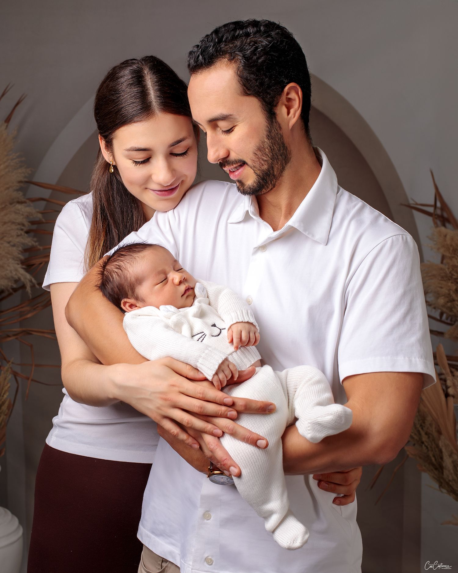 Close up of a mum and dad huddled together smiling holding their newborn baby boy by Caz Captures Sydney Photographer