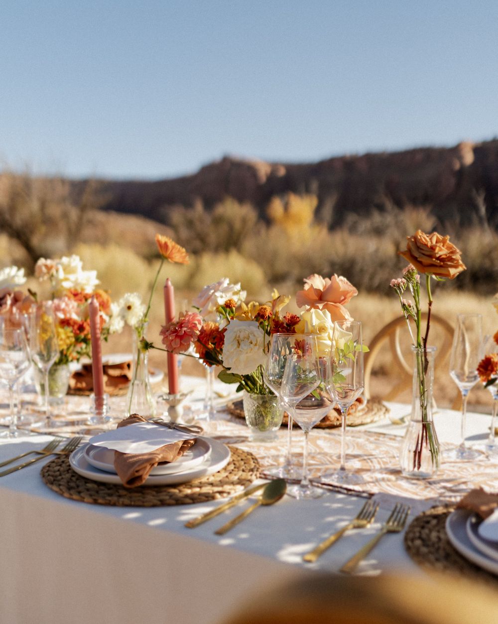 An elegant outdoor table setting with coral flowers and place settings against a desert landscape.