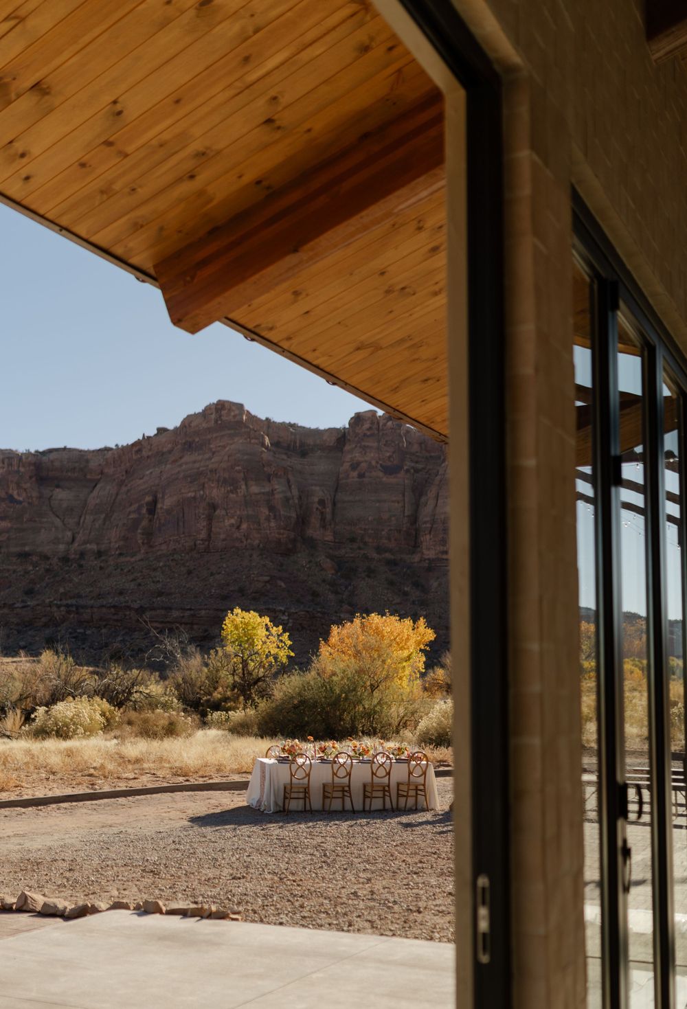 A desert wedding venue setup framed by wooden architecture with red rock cliffs in the background.