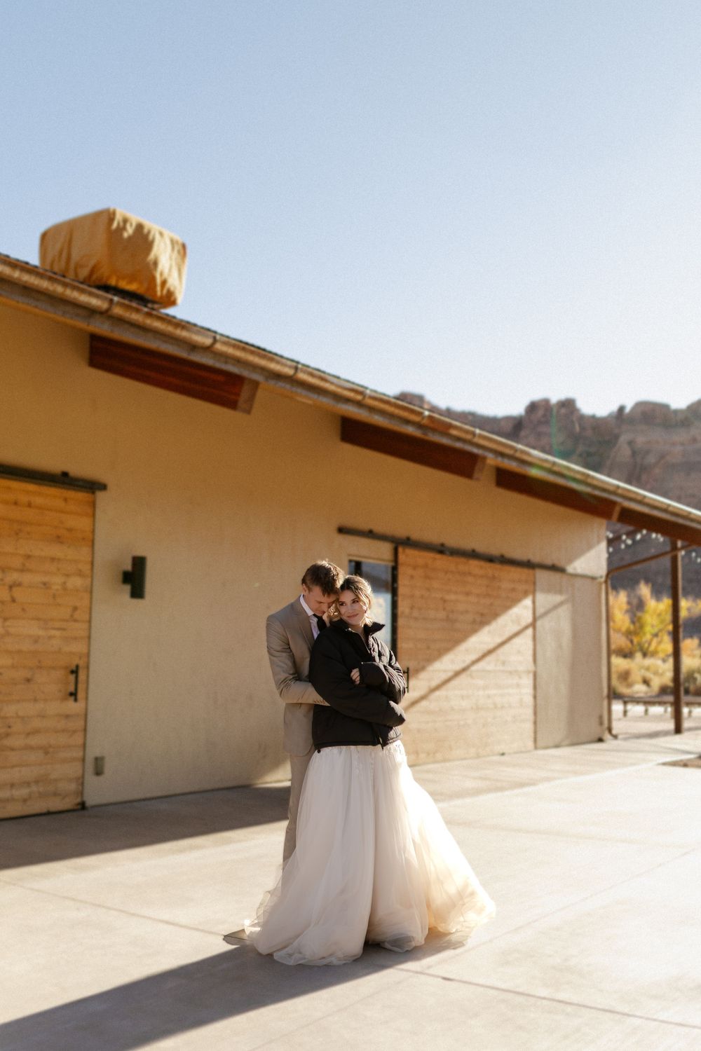 A tender wedding moment captured against a desert building backdrop with mountains in the distance.