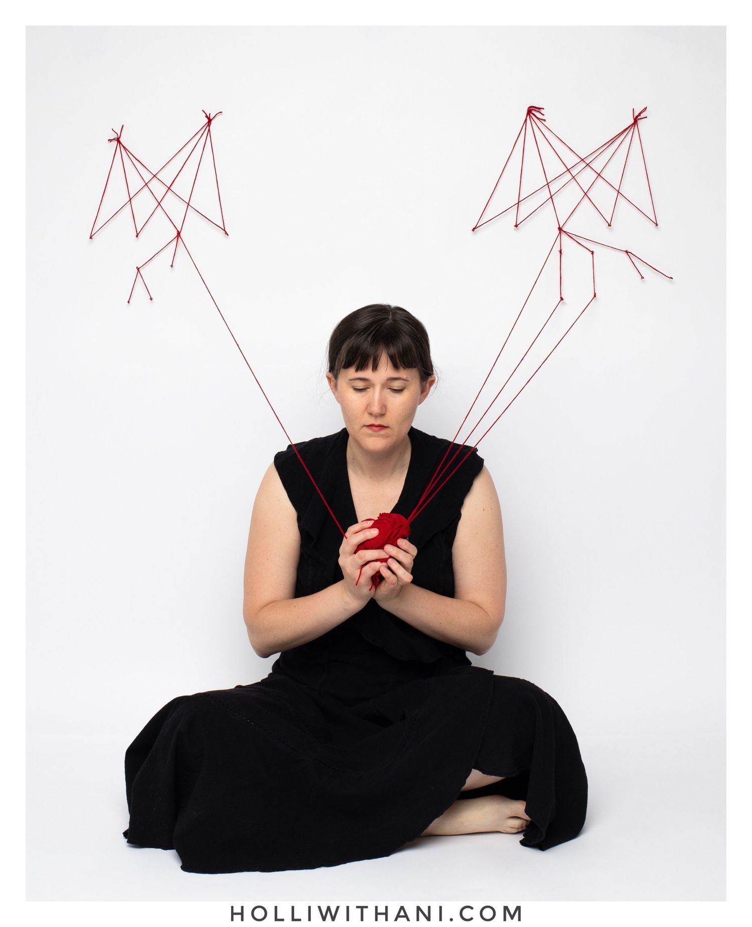 Self-Portrait of woman sitting with black dress, red strings by Holli Margell