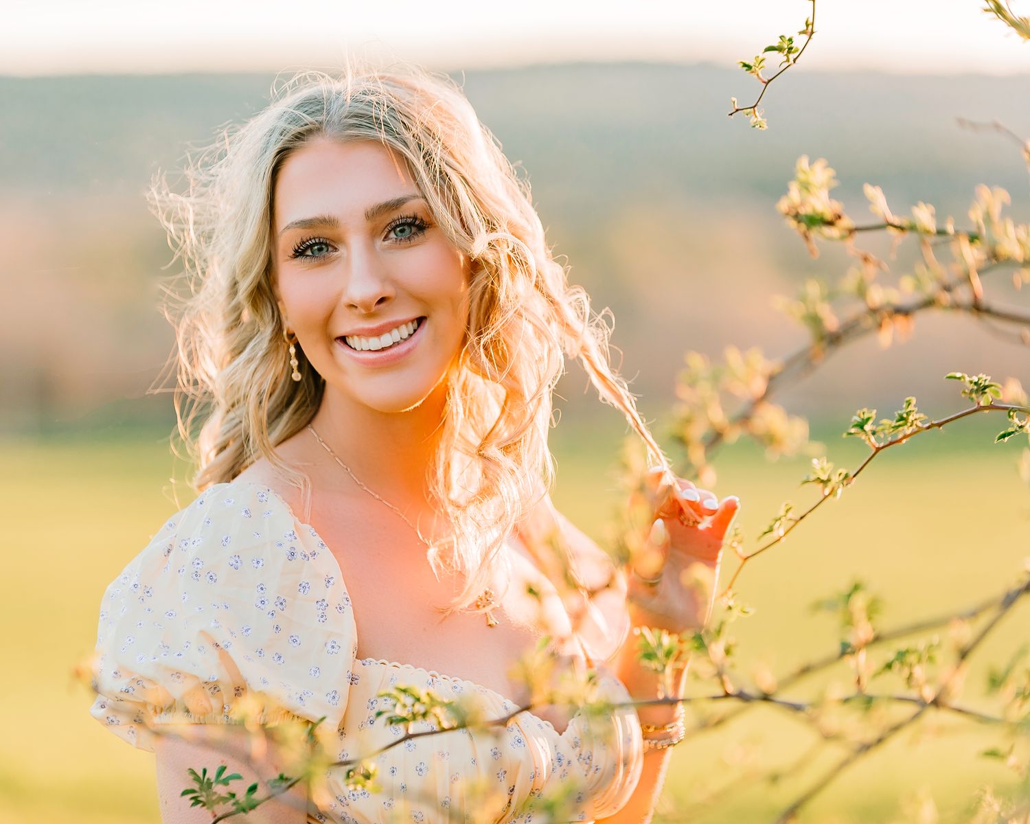 A portrait taken in the spring of a Senior Teen in golden light wearing a floral yellow dress and playing with her hair.