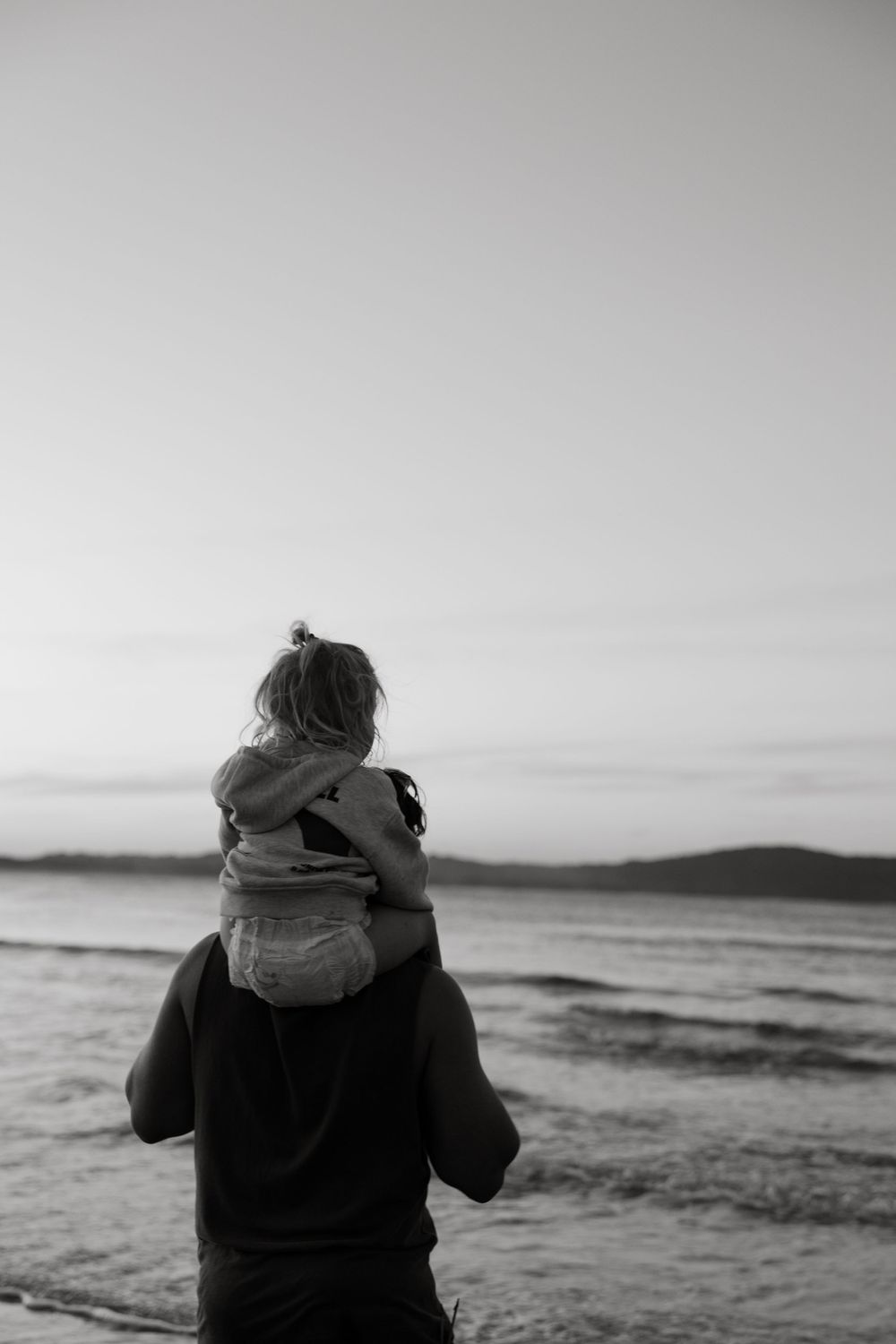 Silhouetted figures against ocean horizon in dramatic black and white photography.
