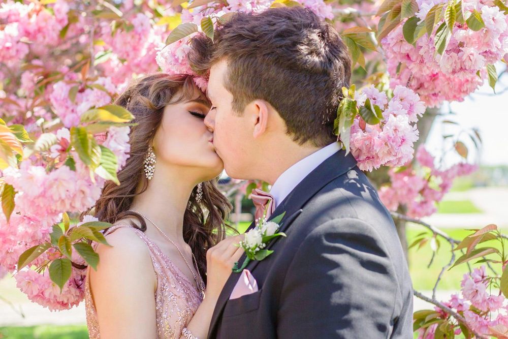 Prom couple kissing while surrounded by pink cherry blossom trees in Yarmouth, Nova Scotia