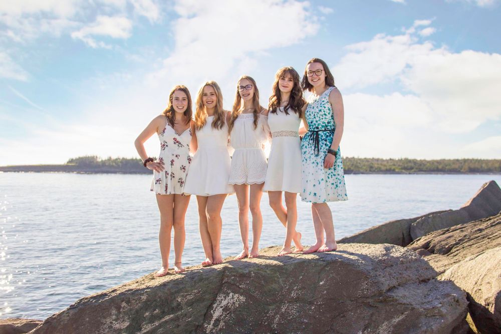 Group of girls posed in front of the ocean for graduation photos in Yarmouth, NS