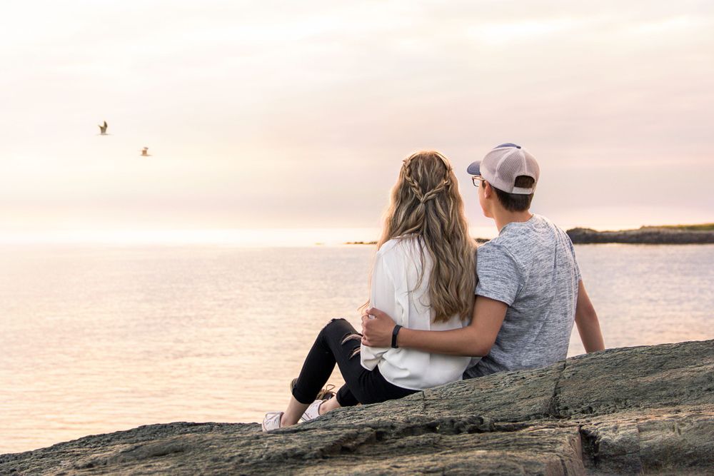 Couple sitting on a rocky ledge overlooking a beautiful sunset in Yarmouth by portrait photographer Daneesha Williams