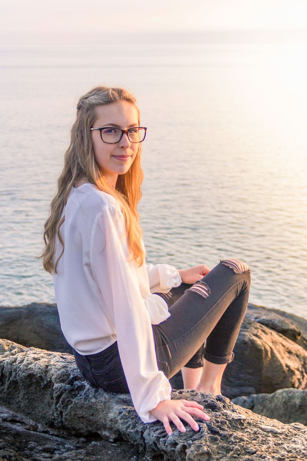 A girl sitting on a rocky ledge overlooking the ocean in Yarmouth by portrait photographer Daneesha WIlliams