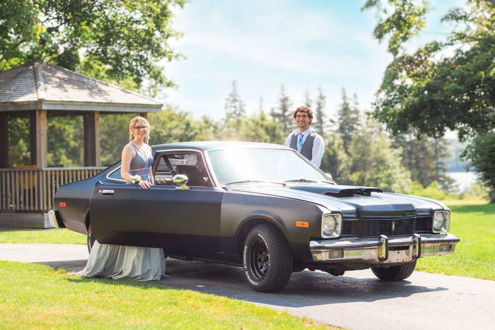 Prom photo of a couple standing with their black vintage car on a sunny day in Yarmouth, NS