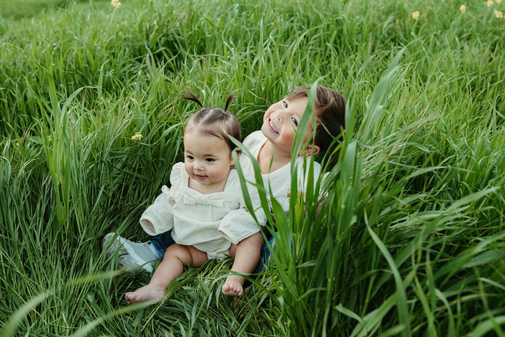Small child sits playfully in tall green grass on a sunny day  at Antioch, CA