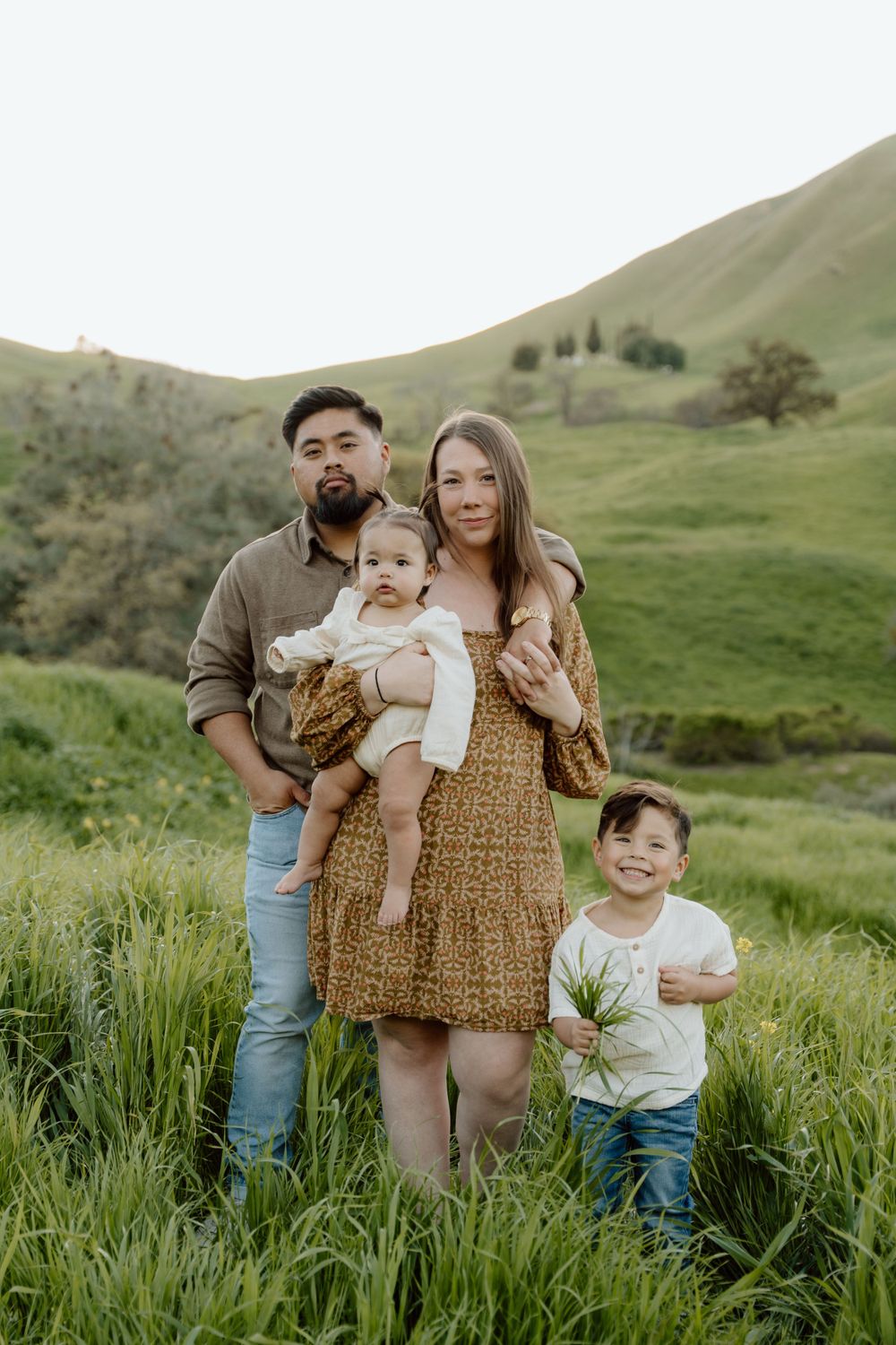 Family standing together in tall grass with rolling green hills in the background at Antioch, CA