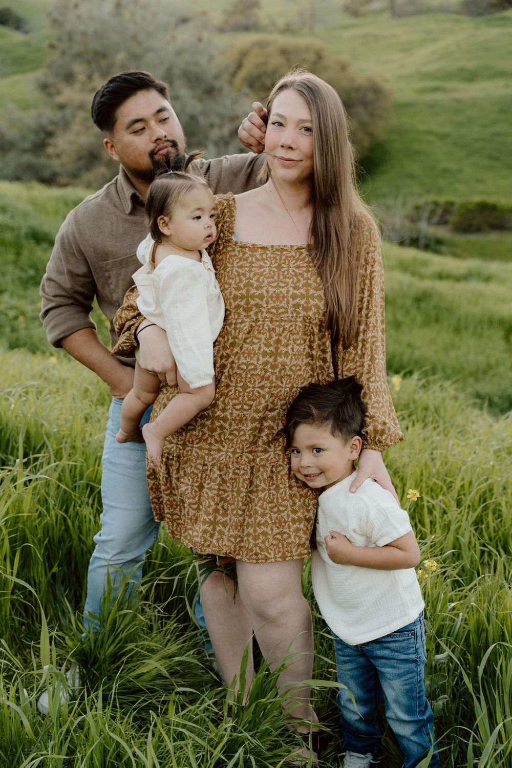 Family portrait in golden light with rolling hills and green grass surrounding them at Antioch, CA.
