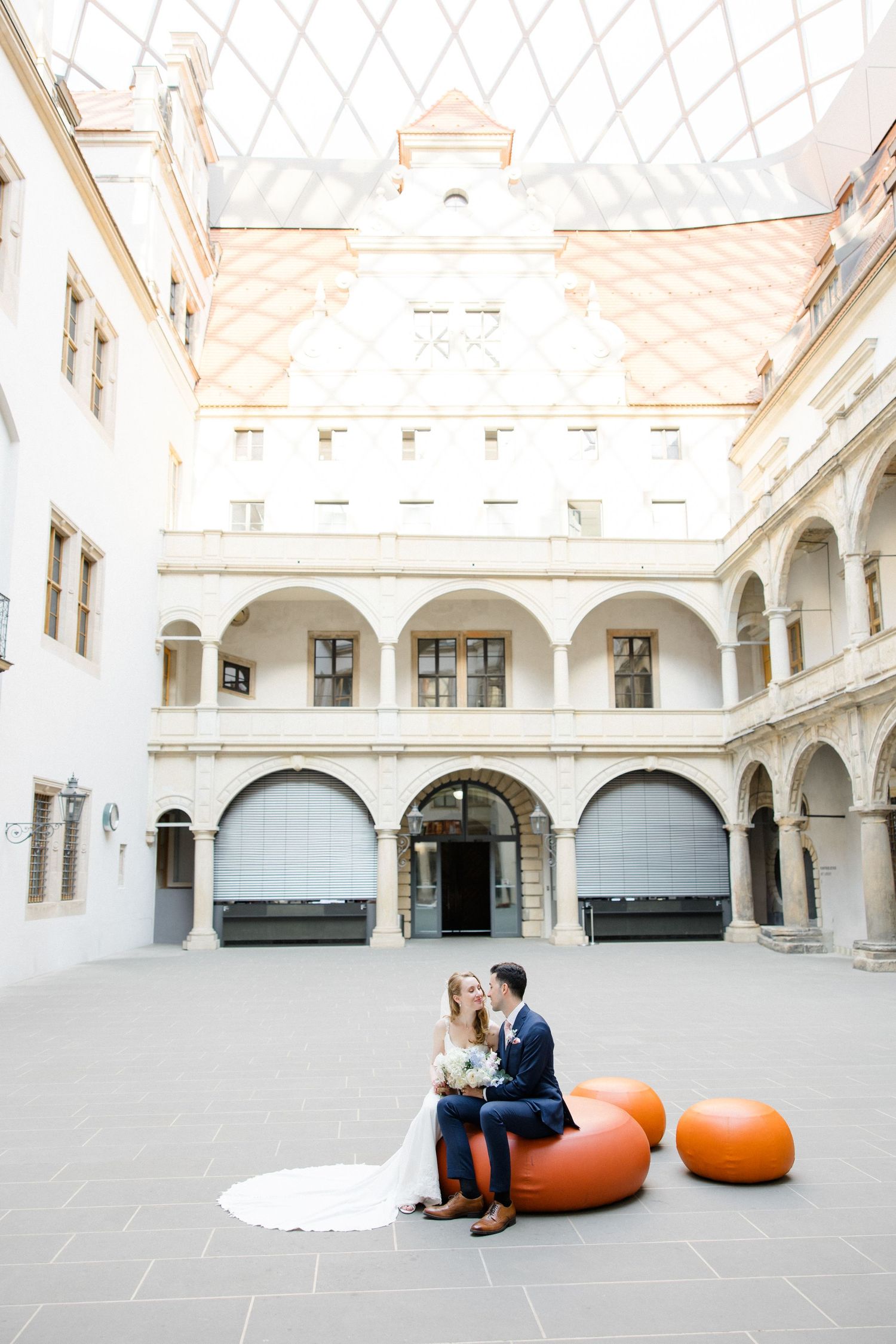 Interior courtyard of historic white building with couple sitting on orange poufs. Organized wedding by MyCastleWedding | Dresden.