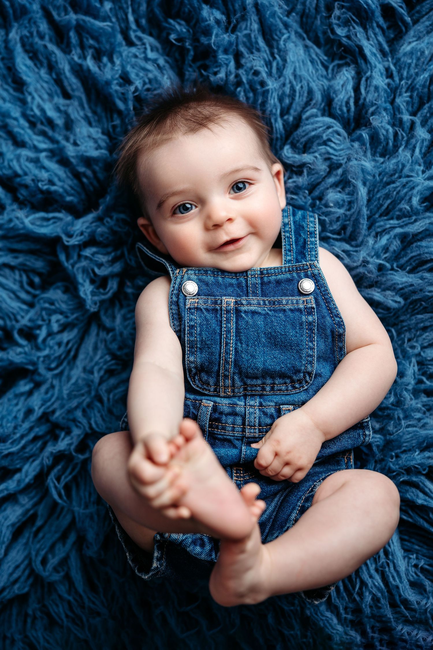 Three month old baby in denim overalls on blue flokati Middle TN milestone photographer.
