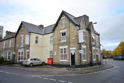 Corner view of a Victorian stone building with cream painted sections and parked cars.