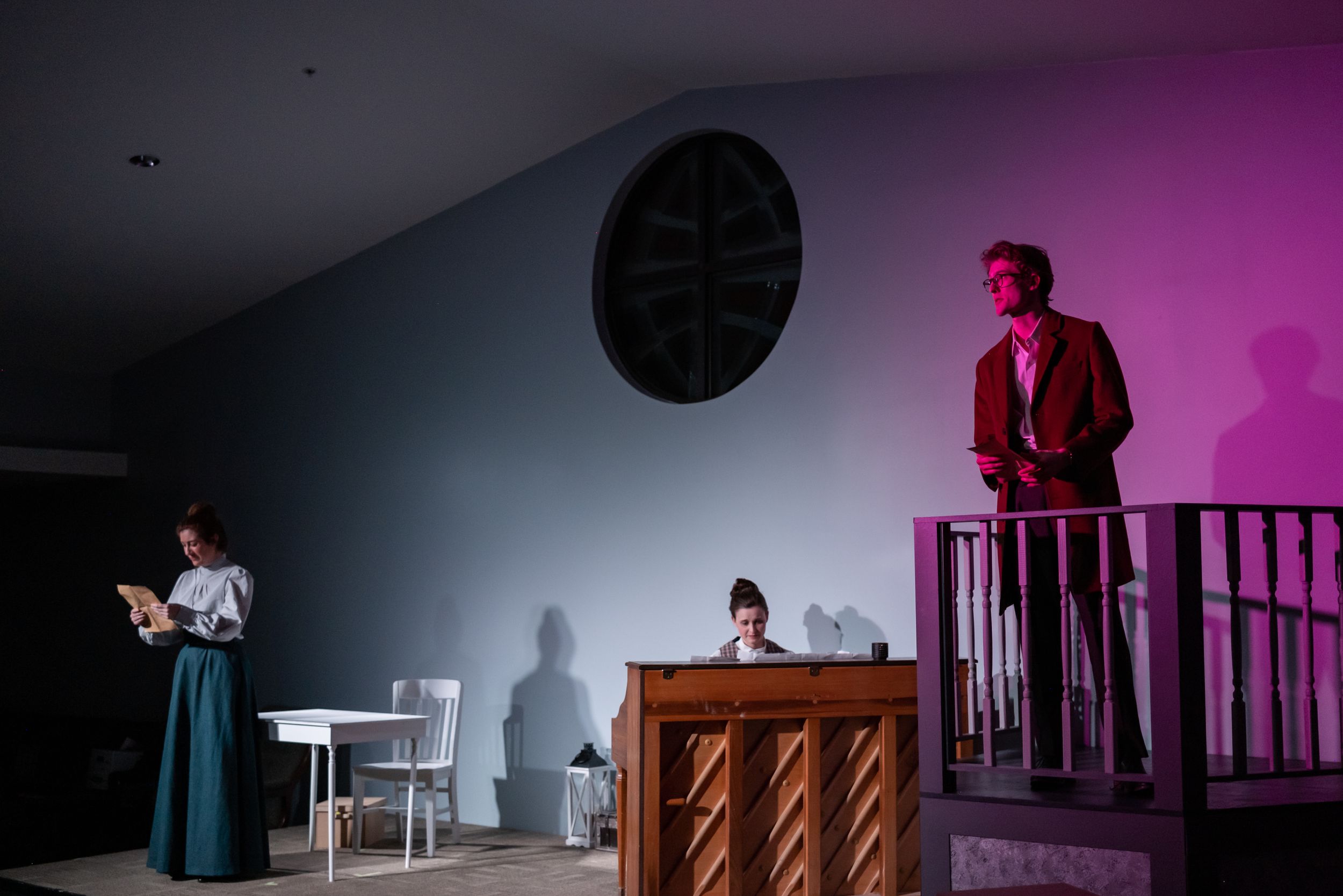 Theater stage scene with dramatic lighting showing performers in period costumes on different levels.