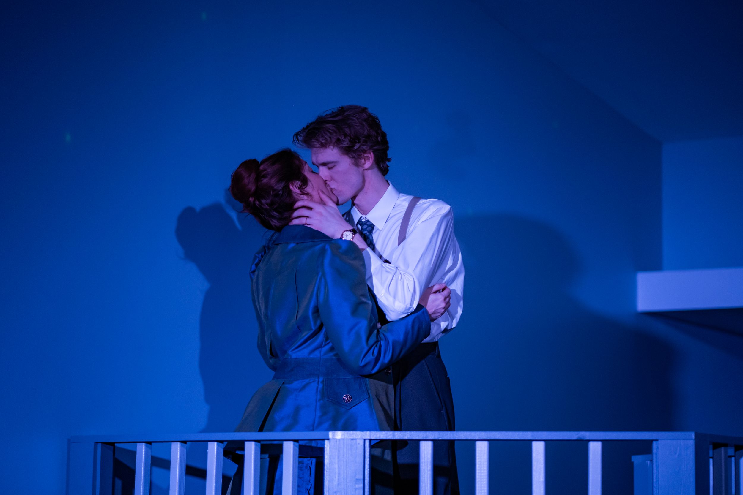 Romantic scene between two performers on a balcony with deep blue lighting.