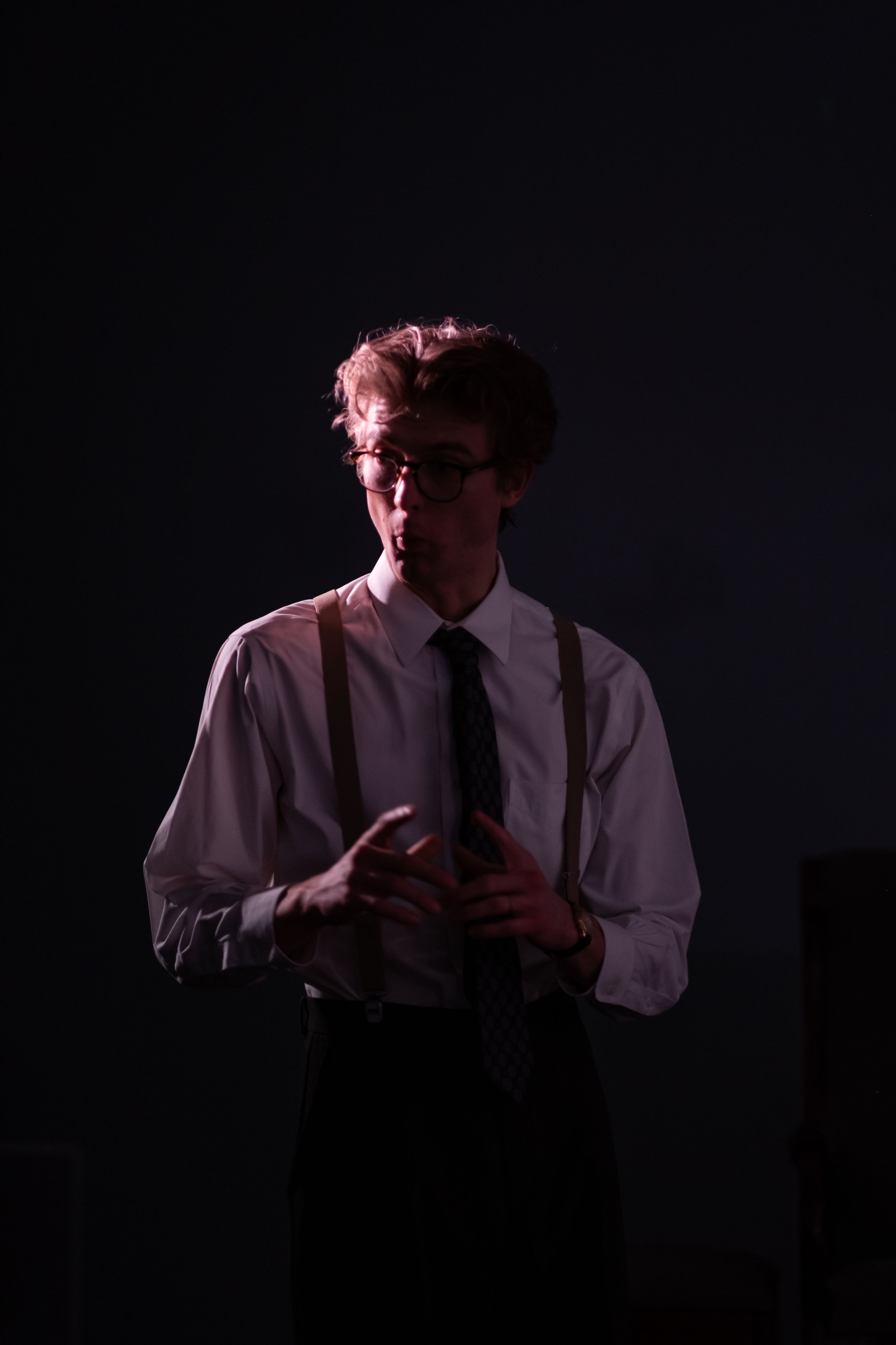 Dramatic silhouette of performer in suspenders and tie against dark background.