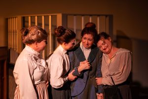 Group of performers in period costumes sharing a lighthearted moment on stage.