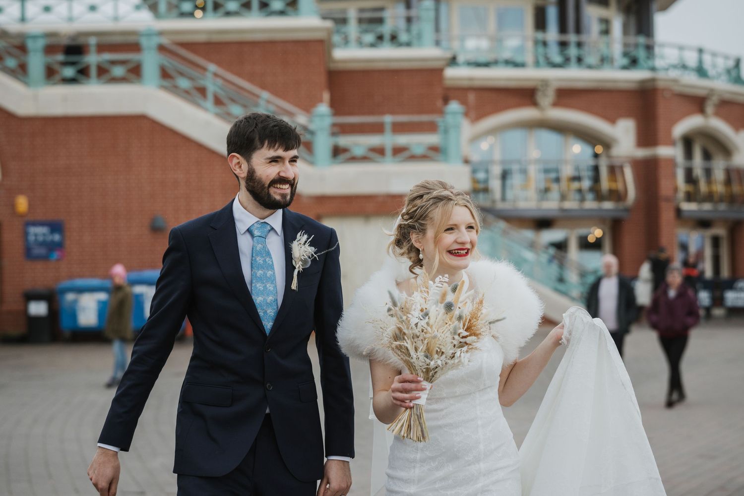 Bride and groom smiling and walking, the bride holding a bouquet of dried flowers, wearing a white dress