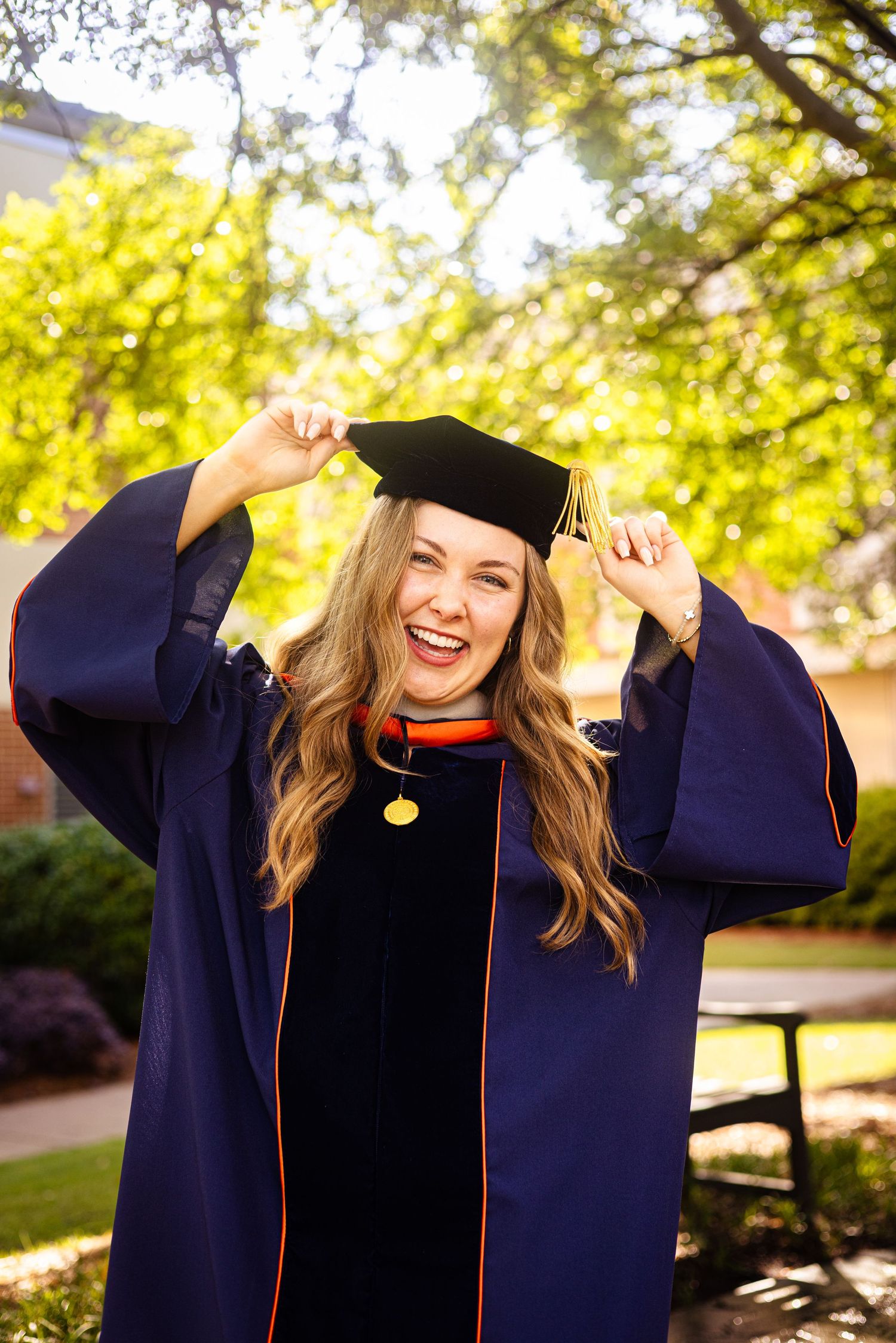 Graduation poses with hands on cap in outdoor greenery in Auburn Alabama.