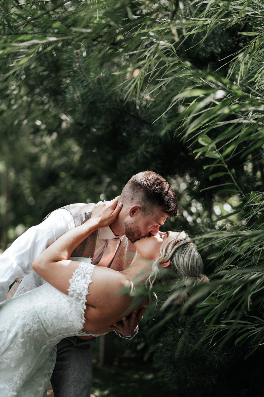 Bride and groom kissing among greenery.